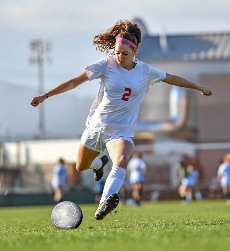 A female soccer player kicking the ball.
